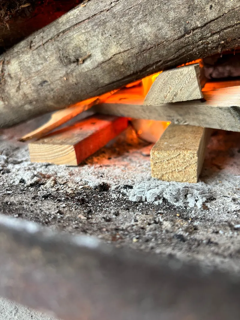 Nahaufnahme des Anzündholzes unter den Scheiten, darunter Asche vom letzten Feuer