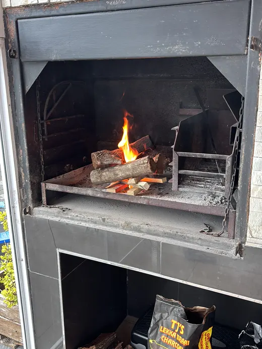 A built braai with a wood fire burning, the wood store with logs and charcoal beneath it