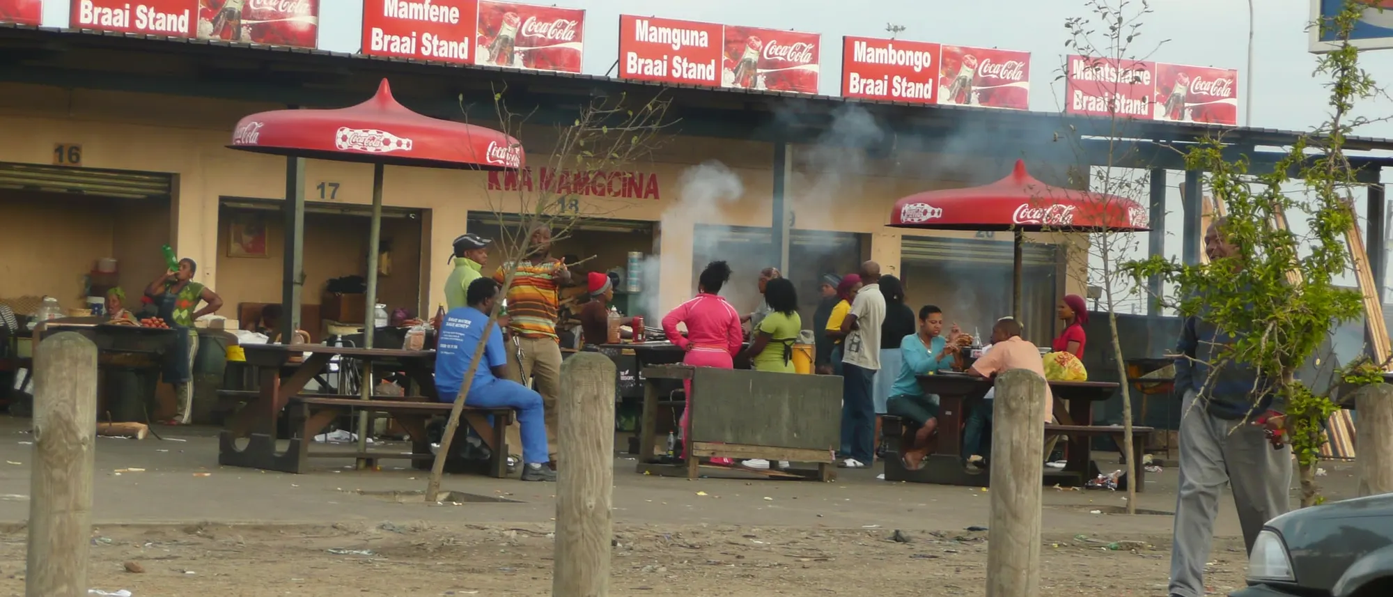 Braai-Stände an einer Straße in Khayelitsha, Kapstadt, mit Gästen an langen Tischen