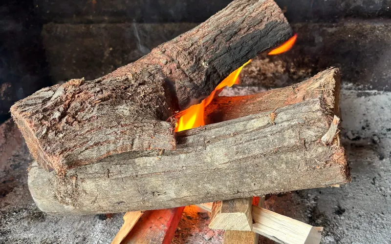 Kindling under two heavy logs, the flame just catching
