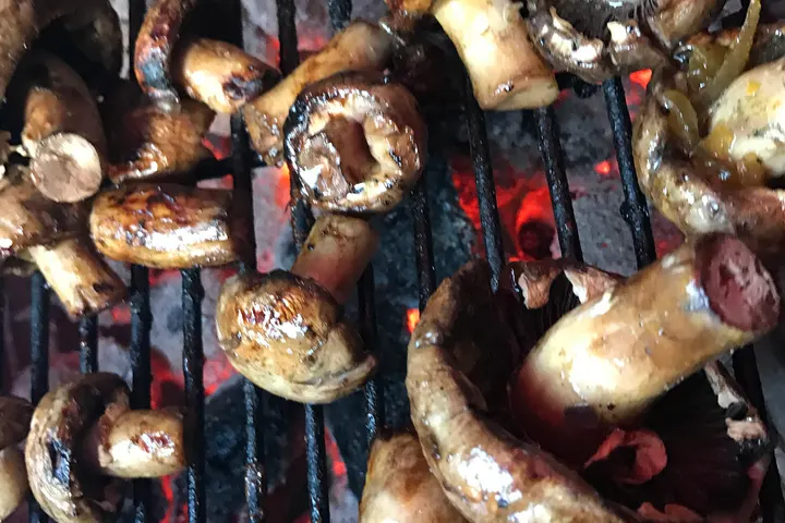 Große Champignons neben Wors auf dem Rost über der Glut