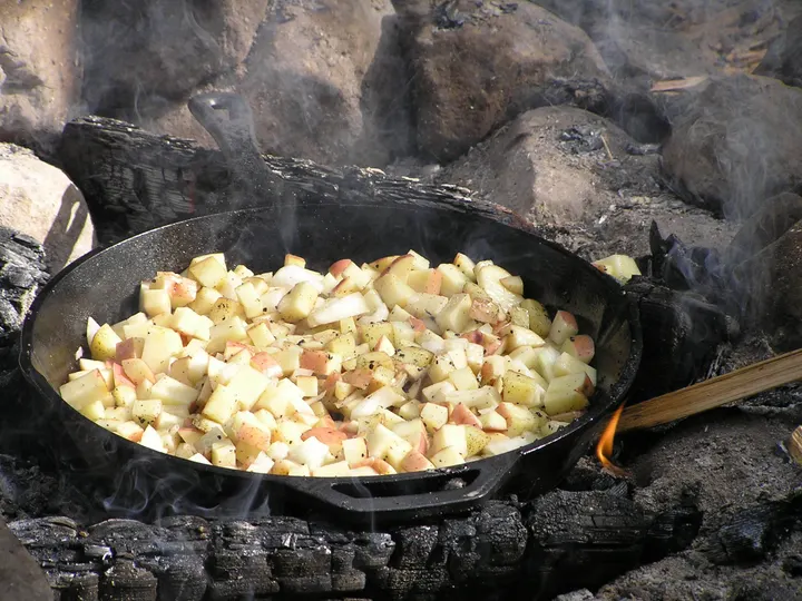 Gusseiserne Pfanne mit gewürfelten Kartoffeln auf brennenden Scheiten