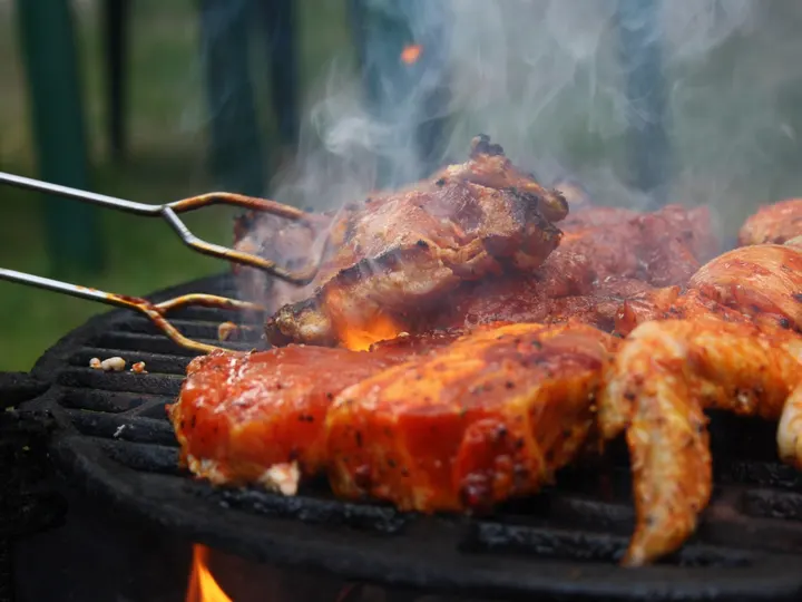 Lange Metallzange fasst ein Stück Fleisch auf dem rauchenden Rost