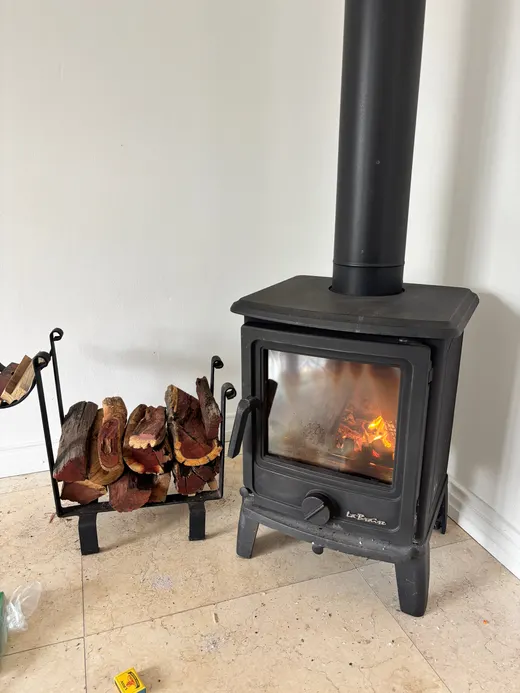 A cast-iron wood stove with a fire burning, a rack of logs beside it