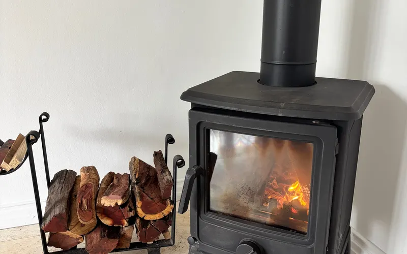 A cast-iron wood stove with a fire burning, a rack of logs beside it