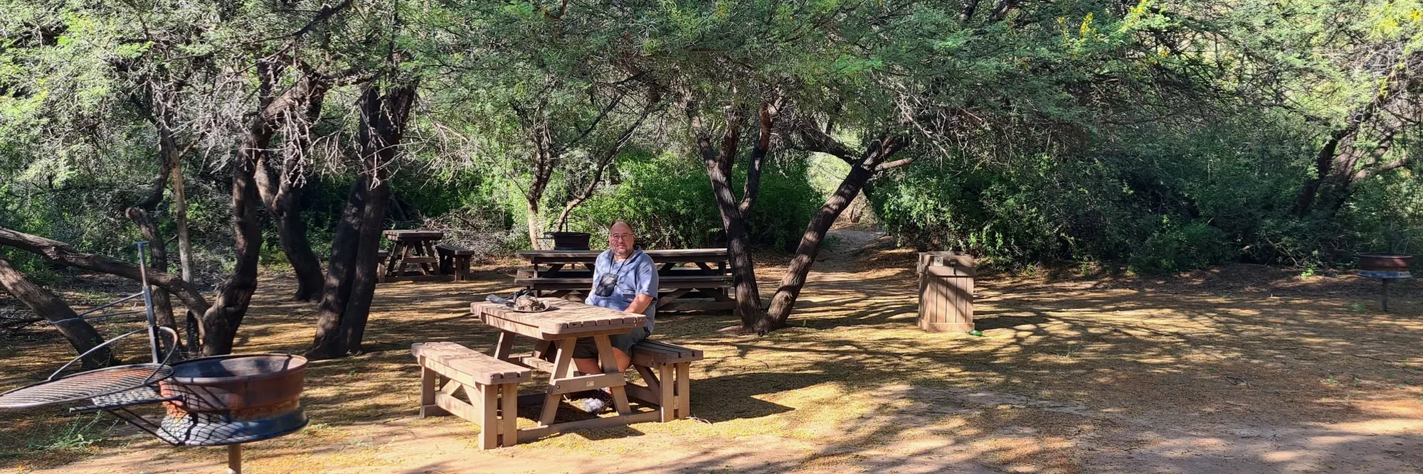 Picknickplatz im Karoo-Nationalpark: Holztische unter Dornbäumen, davor eine Feuerschale mit ausschwenkbarem Rost