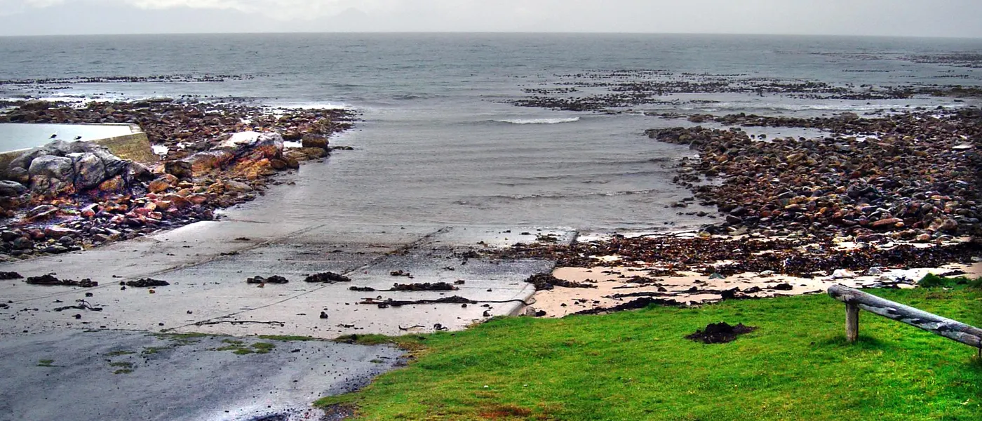 Betonslipway und Rasenfläche an der Bucht von Buffels Bay, davor die felsige Küste