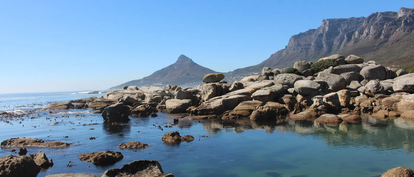Runde Granitfelsen und flaches Wasser an der Küste von Oudekraal, dahinter der Lion's Head