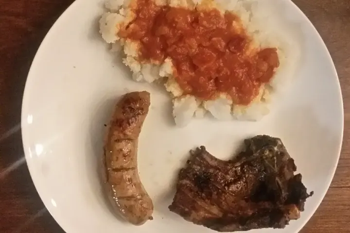 Teller mit Stywe Pap, Sheba-Sauce, Wors und einem Lammkotelett