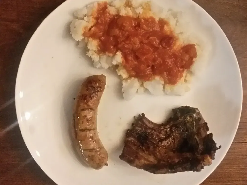 Teller mit Stywe Pap, Sheba-Sauce, Wors und einem Lammkotelett