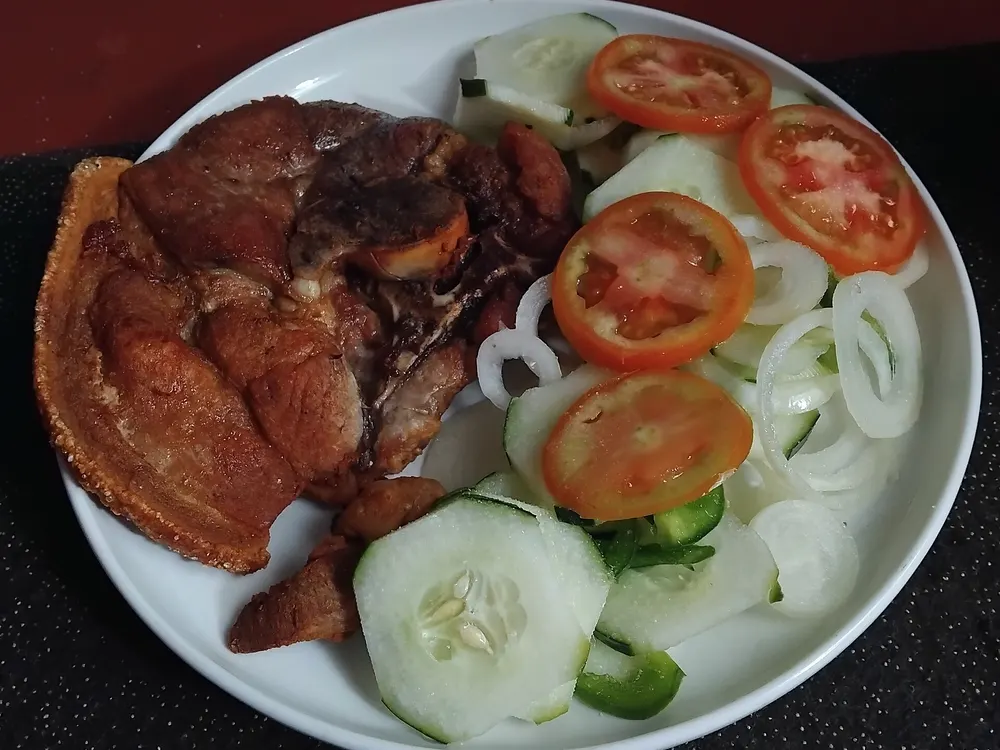 Gebratener Schweinebauch mit knuspriger Kante, dazu Tomaten- und Gurkenscheiben