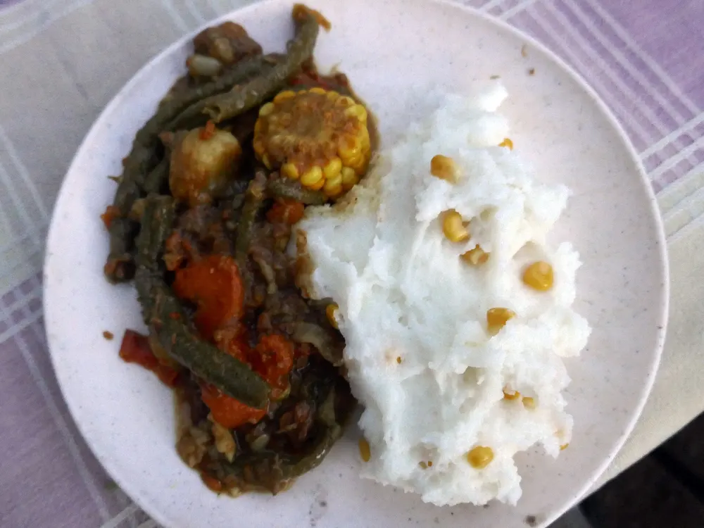 Gusseiserner Dreibeintopf mit Eintopf, daneben eine Portion Pap