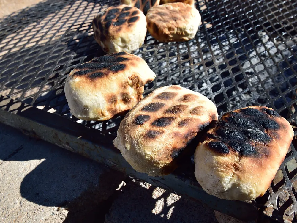 Roosterkoek auf dem Rost über der Glut, mehrere Teiglinge nebeneinander