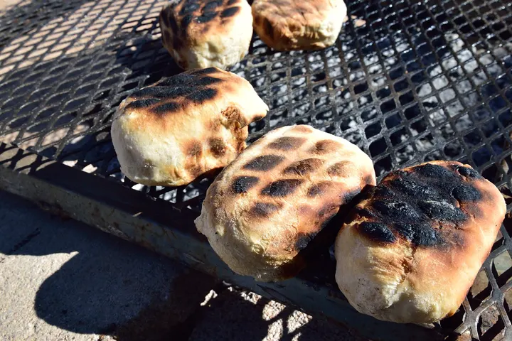 Roosterkoek auf dem Rost über der Glut, mehrere Teiglinge nebeneinander