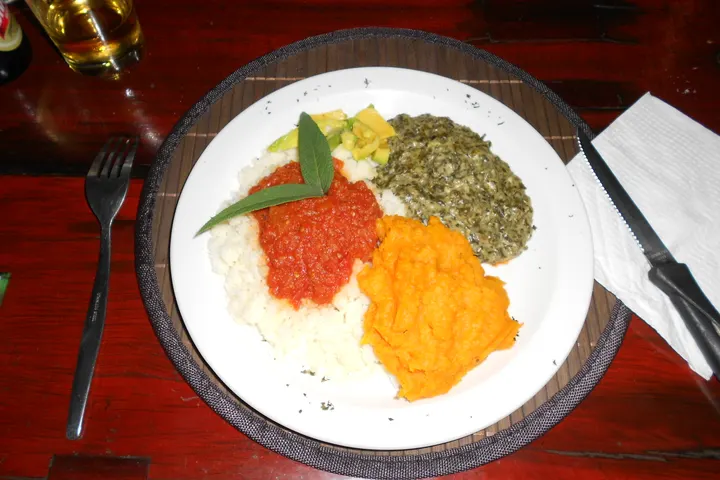 Teller mit Pap, roter Tomatensauce, Kürbis und Spinat