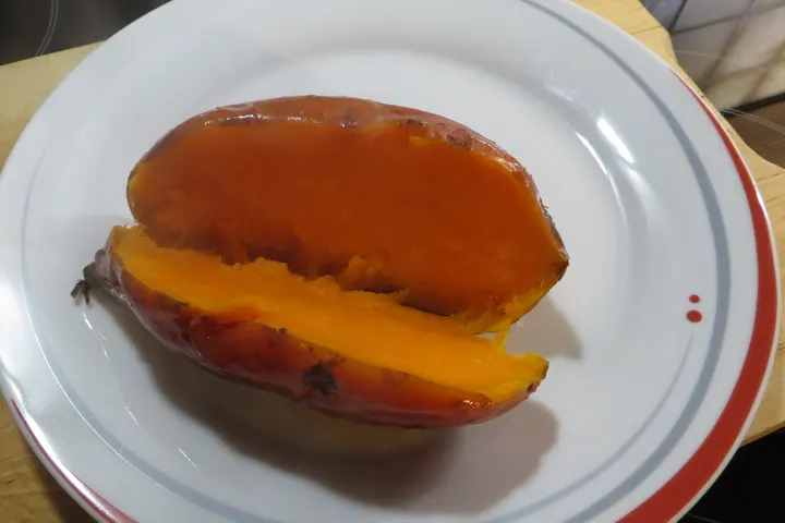 Gebackene Süßkartoffel, längs aufgerissen, das Fleisch leuchtend orange
