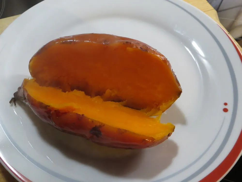 Gebackene Süßkartoffel, längs aufgerissen, das Fleisch leuchtend orange