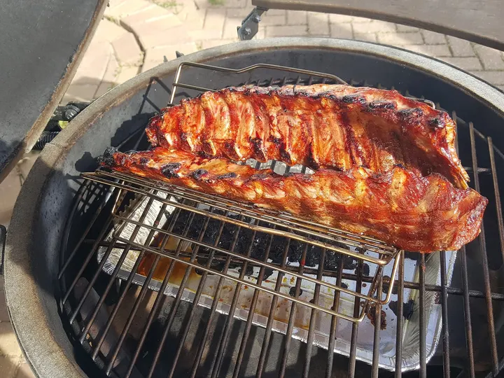 Ein Rippenbogen auf erhöhtem Rost über einer Tropfschale im runden Grill, Deckel aufgeklappt