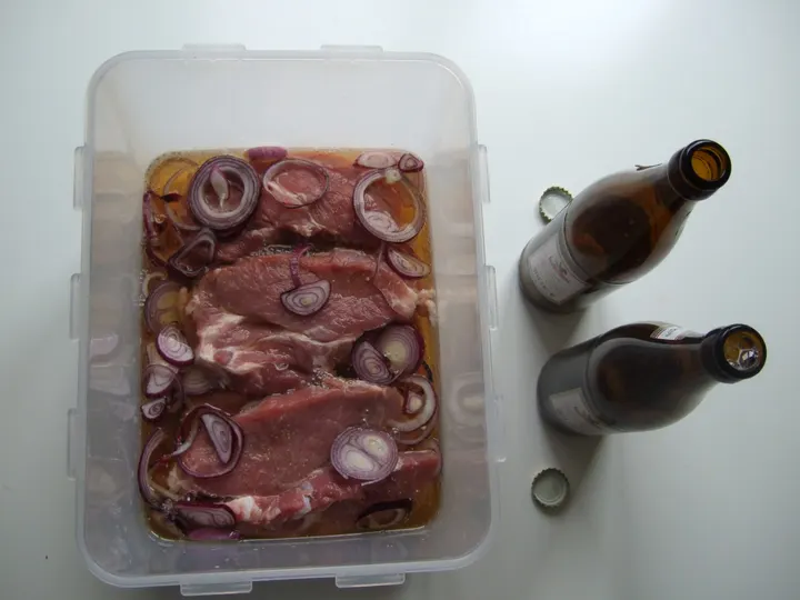 Schweinesteaks mit roten Zwiebelringen in einer Biermarinade in einer durchsichtigen Dose