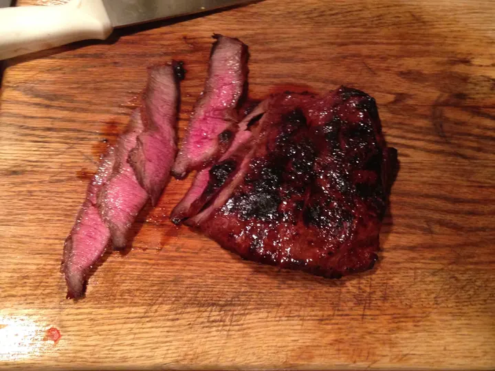Ein gegrilltes Flankensteak, angeschnitten auf dem Brett, drei rosa Scheiben daneben