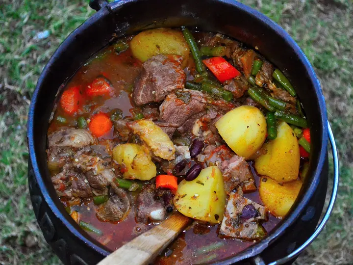 Von oben in den offenen Dreibeintopf: Fleisch, Kartoffeln, Möhren, grüne Bohnen und Paprika in Lagen