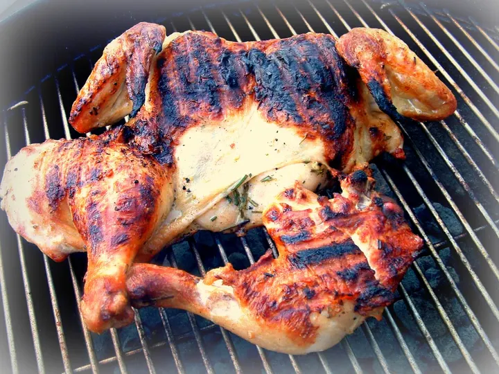 Ein flach aufgeklapptes ganzes Hähnchen mit dunklen Streifen vom Rost