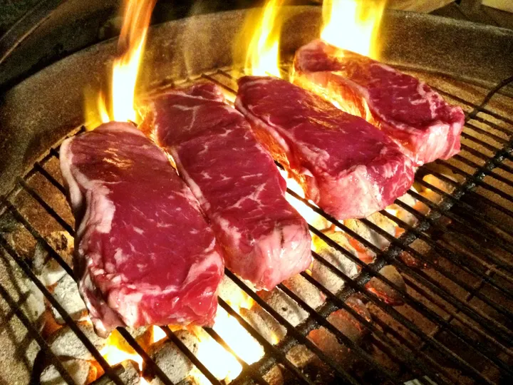 Hohe gelbe Flammen schlagen zwischen vier rohen Rindersteaks aus der Glut hoch