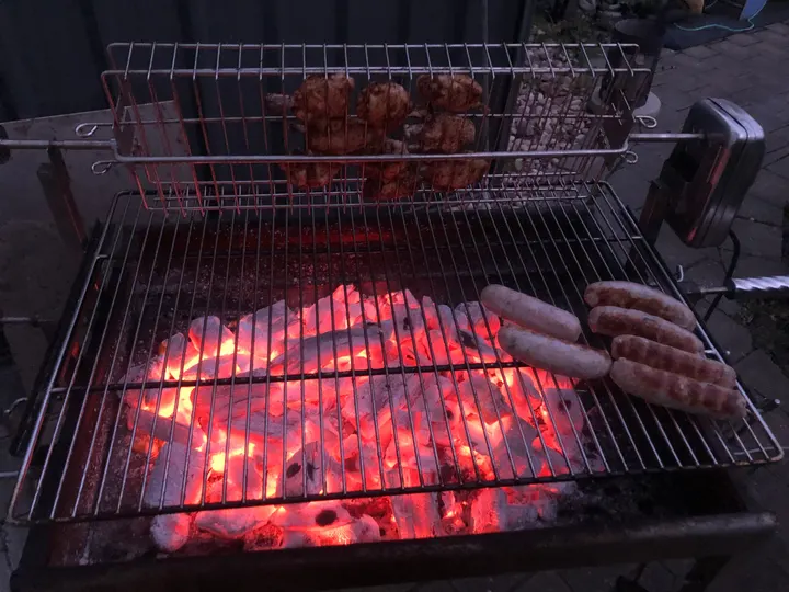 Glühende Kohle auf der linken Grillhälfte, rechts liegen die Würste über der freien Fläche